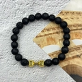 Close-up of black volcanic lava beads with a gold dumbbell charm and engraved words - Lava Stone Gold