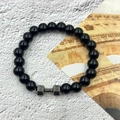 Polished black bead bracelet with a matte grey dumbbell charm on stone background - Glossy Stone Gunmetal