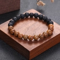 Handmade beaded bracelet with black lava stone and natural wood beads on a wooden stand - Lava Stone + Wood Grain
