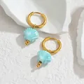 Macro view of ocean style 18K gold earrings with blue shell pendants on white stone - Turquoise Blue