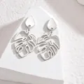 Detailansicht der silbernen Edelstahl-Ohrringe mit Monstera-Blatt auf weißem Stein - Wassertropfen-Stil / Stahlfarbe