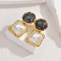 Détail de boucles d'oreilles dorées avec cabochon marbré et accents nacrés de style rétro - Noir