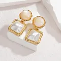 Detailansicht vergoldeter geometrischer Perlenohrringe auf minimalistischem Steinsockel - Creme