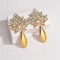 Detailansicht vergoldeter Blumenohrringe mit Kristallen auf weißem Steinuntergrund - Weiße Strass (S-E986-bai)