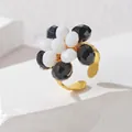 Detail eines Perlen-Blumenrings mit schwarz-weißen Steinen auf goldenem offenem Ring - Schwarz & Weiß