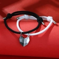 Black and white woven couple bracelets with magnetic half-heart charms on red background - Black And White Cord With Black And Silver Heart
