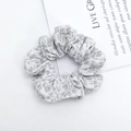 Dettaglio di un elastico per capelli in tessuto grigio a fiori con texture a pieghe - Grigio