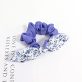 Vue détaillée d'un chouchou en tissu violet avec nœud à fleurs bleues sur fond blanc - Style Floral Blanc Bleu Patchwork Violet
