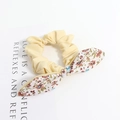 Chouchou en tissu jaune pâle avec nœud floral sur un fond blanc épuré - Style Floral Patchwork Jaune Oie