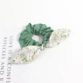 Détail d'un chouchou vert avec nœud floral et carte décorative sur fond blanc pur - Style Floral Vert Patchwork Vert Foncé