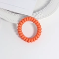 Detailansicht eines matten orangefarbenen Spiralhaargummis auf einem weißen Zierteller - Farbe 10