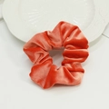 Chouchou en velours orange corail vif présenté sur une assiette blanche texturée - Orange
