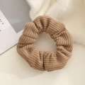 Close-up detail of a brown knitted scrunchie showing fine ribbed wool texture on white plush - Brown