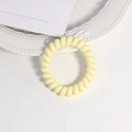 Detail eines gelben Spiralhaargummis im Telefondraht-Stil auf weißem Keramikteller - Farbe 11
