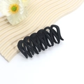 Close-up of a matte black wavy hair claw clip displayed on a minimalist beige wave plate - Intertwined Wave Design