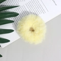 Dettaglio di un elastico per capelli in peluche giallo chiaro su sfondo decorativo - Giallo