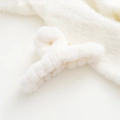 Detail of soft cream faux fur hair claw clip on matching textured knit fabric background - White