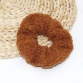 Detailed view of brown plush lamb velvet hair scrunchie on a woven straw mat - Brown