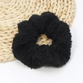 Close-up of black fuzzy lamb wool scrunchie with soft plush texture on a woven mat - Black