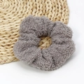 Close-up of a grey fuzzy lamb wool scrunchie showing its soft texture on a woven mat - Gray