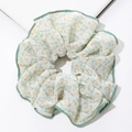 Detail eines geblümten XL-Haargummis mit gelbem Print und grünem Saum auf Weiß - Grün