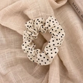 Dettaglio di uno scrunchie color crema a pois su sfondo di lino con luce morbida e calda - Piccolo