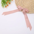Detailed view of pink satin long tail bow hair clip on a woven mat with orange flowers - Lotus Pink