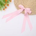 Close-up of a pink satin double-layered bow hair clip with long ribbons on a woven basket - Pink