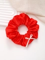 Détail d'un chouchou en satin rouge brillant orné d'un délicat nœud en ruban de couleur crème - Rouge