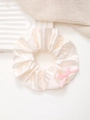 Détail d'un chouchou en satin champagne avec un nœud rose sur un plateau texturé - Blanc