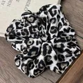 Retro Haargummi mit Leopardenmuster, Seidentextur auf Holztisch und Buch-Hintergrund - Schwarz-Weißer Leopardenprint
