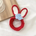 Handmade red crochet bunny ear hair tie with a blue flower accent on a wood tray - Red