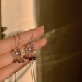 Detail of rose gold tassel earrings with moonstone and black pearl drops in warm light - Longevity Lock Style (NST-0012)
