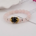 Detailed close-up of pink crystal beads with a golden crown charm on an elegant bracelet - Rose Quartz and Black Agate