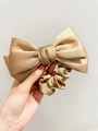 Detailed close-up of champagne gold satin bow scrunchie with elegant silk luster texture - Camel