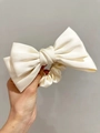 Detail of a creamy white satin bow scrunchie with a silky texture and glossy finish - Off White