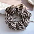 Nahaufnahme eines dicken Strick-Scrunchies mit schwarz-weiß-braunem Chevron-Muster - Braun
