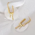 Detail of gold U-shaped earrings with liquid lava texture on white textured background - Gold-Transparent