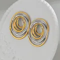 Makroaufnahme von zweifarbigen ovalen Spiralohrringen auf einer weißen Steindekoplatte - Gold und Silber Zweifarbig Unregelmäßig Oval Spirale Stil (S-E897)