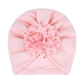 Pink knit baby turban hat with a large gold polka dot floral decoration on white background - Pink