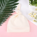 Detalle del gorro con nudo para bebé en punto color crema sobre un fondo decorativo suave - Talla única / Blanco lechoso
