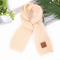 Close-up of cream knit scarf with textured ribbing and brown leather logo patch - Beige