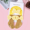 Dettaglio del set cappello e calze neonato in cotone con fiocchi beige su sfondo rosa - Giallo