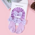Flat lay of purple cotton baby bonnet and matching bow socks on pink background - Purple