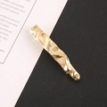 Detail einer goldenen unregelmäßigen Haarspange mit Wellentextur auf diagonalem Grund - Gold