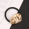 Detailansicht eines goldenen Flüssigmetall-Ornaments auf einem schwarzen Haargummi - Gold