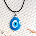Primer plano del colgante de ojo turco de cristal azul con cordón negro sobre fondo de red - Estilo Gota de Agua / 3x4cm / Azul lago