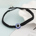 Close-up of black braided evil eye bracelet with blue bead on white shell dish - Black Single Eye (BN-0149-2)