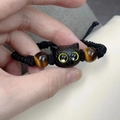 Macro shot of a handmade braided bracelet featuring a black cat carving and tiger eye beads - Yellow-Eyed Cat (BN-0203)