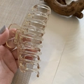 Detail of large amber resin hair claw clip with golden spring held in hand for styling - Champagne